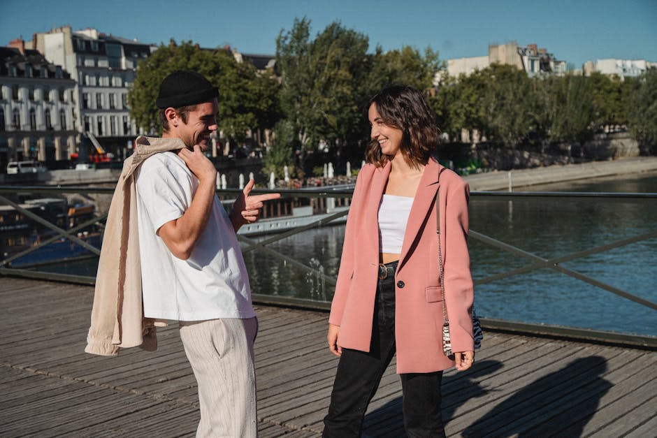 A fashionable couple smiling and interacting on a sunny day by the river.