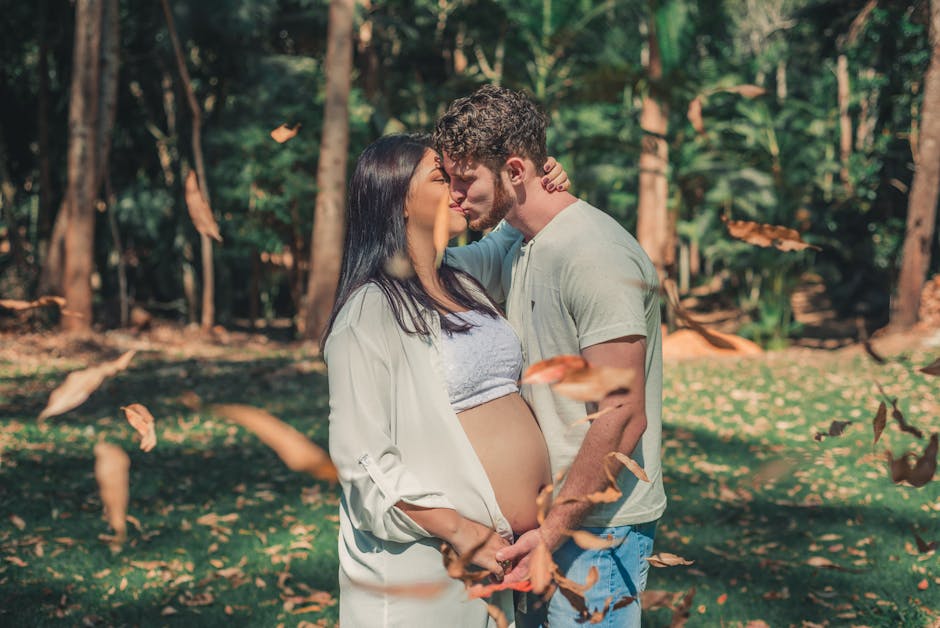 Young couple sharing a tender moment in an outdoor setting surrounded by trees and falling leaves.