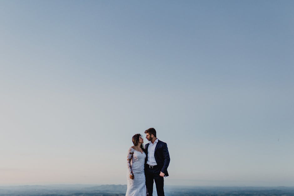 Bride and groom embracing outdoors under a clear blue sky.