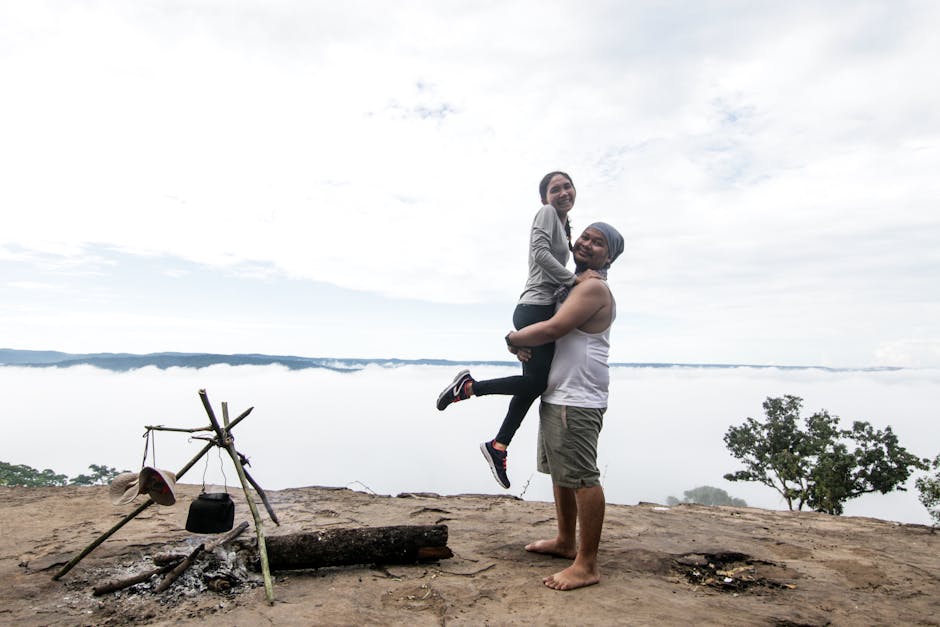 A joyful Asian couple embraces at a campsite overlooking a scenic view in Cambodia, capturing the essence of outdoor adventure.