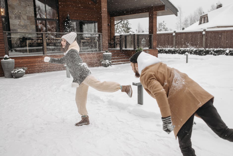 A joyful couple playing in the snow outside a wooden house during winter.