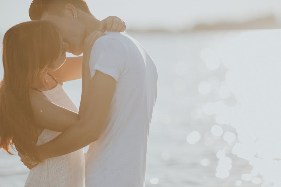 A couple shares a tender moment by the sunlit water, capturing an intimate embrace.