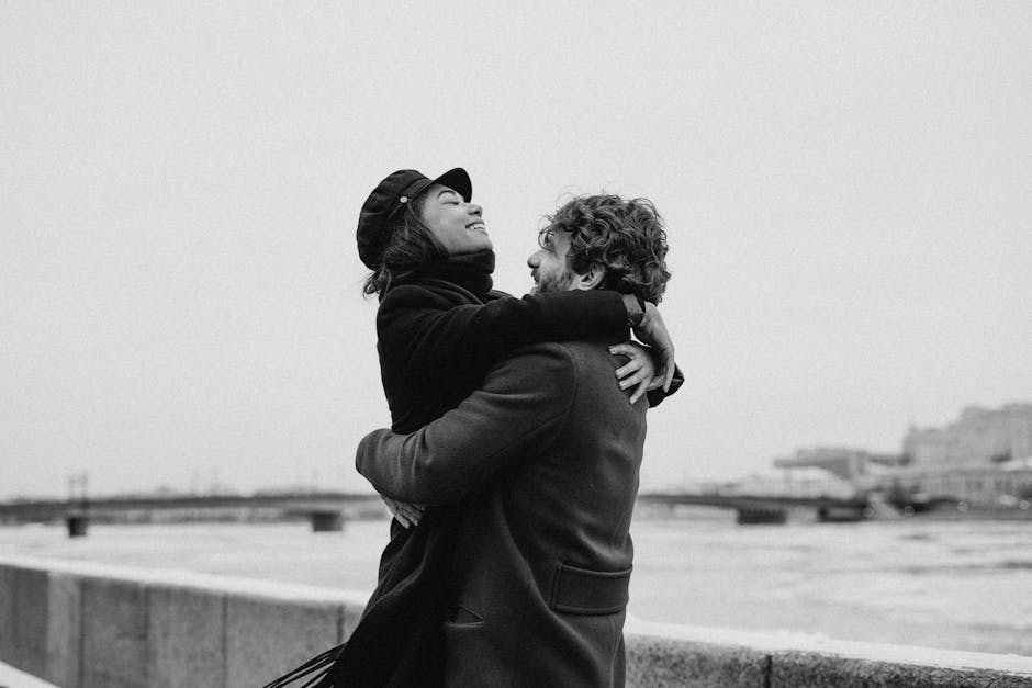 A joyful couple embracing by the seaside in a monochrome winter setting, expressing happiness and romance.