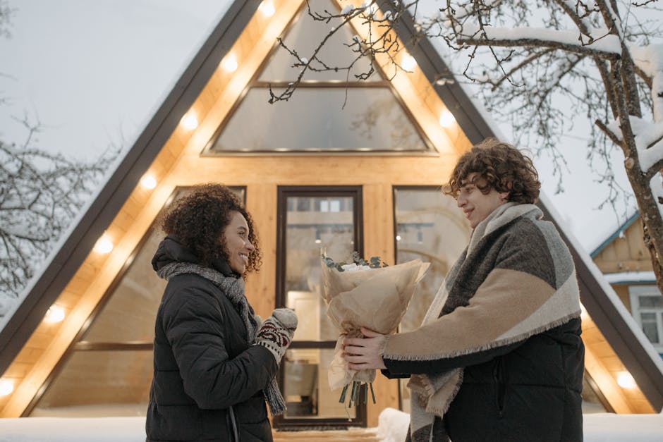 A couple sharing a romantic moment in front of a winter cabin with a bouquet exchange.