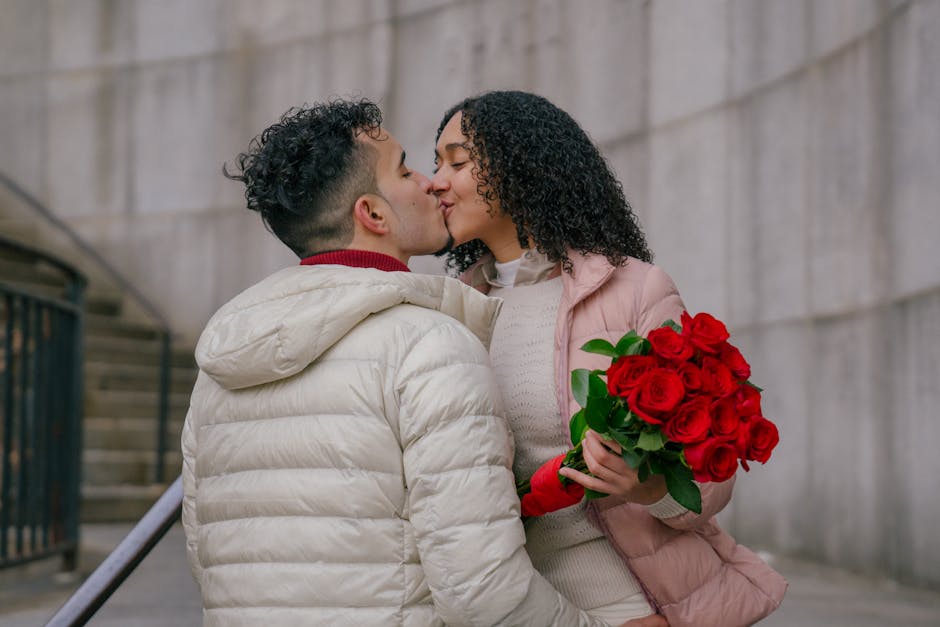 Loving ethnic couple with bouquet of bright blooming roses kissing each other on urban street