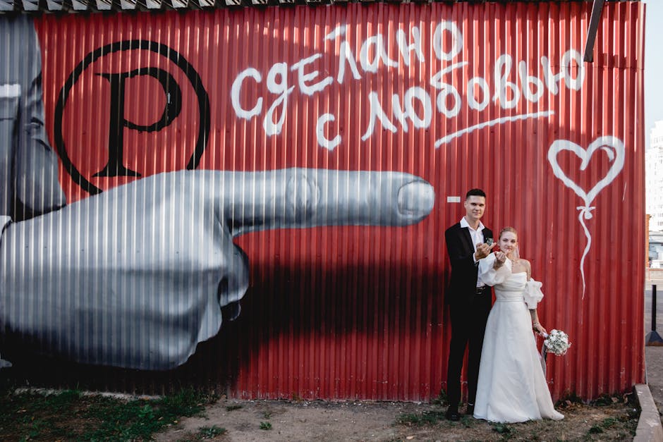 Bride and groom pose by colorful graffiti with a heart on a red wall.