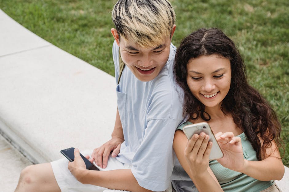 A cheerful couple enjoying free time together, browsing on smartphones while sitting on a park bench.