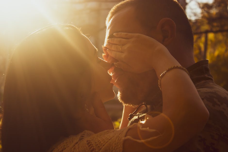 A couple shares an intimate kiss in warm, golden sunlight outdoors, evoking love and romance.