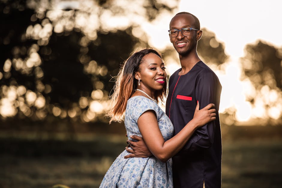 Smiling African American couple embracing outdoors with a bright bokeh background, expressing love and joy.