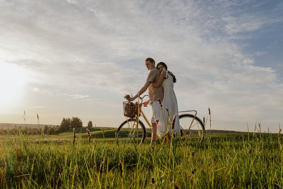 A couple embraces with a bicycle in a sunny meadow, exuding love and warmth.