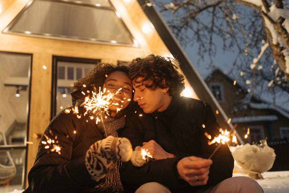 Happy couple holding sparklers outside a cozy cabin in winter, creating a festive atmosphere.