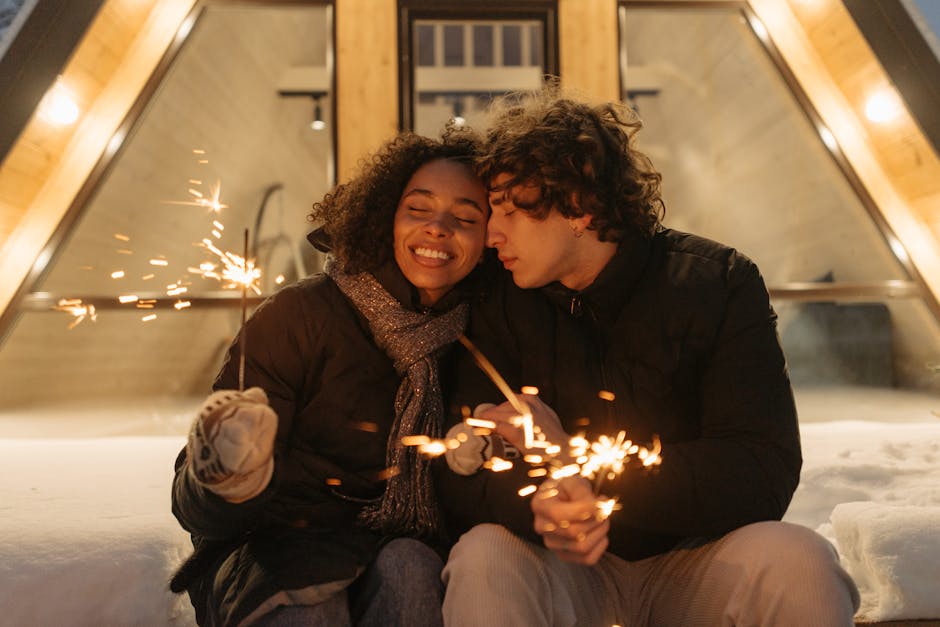 A joyful couple enjoying sparklers outside a cozy cabin in winter attire.