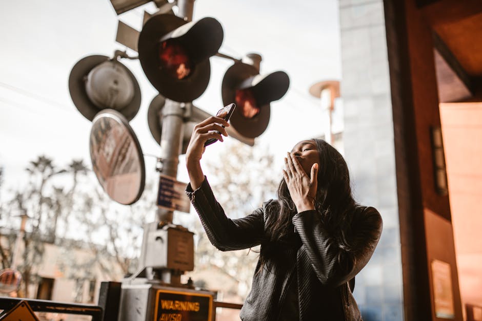 A woman takes a selfie near an urban railway crossing, expressing excitement and connection.