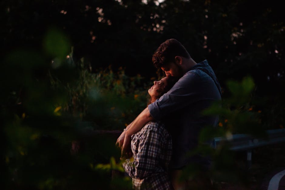 A couple shares a tender embrace in a peaceful forest at sunset, surrounded by nature.