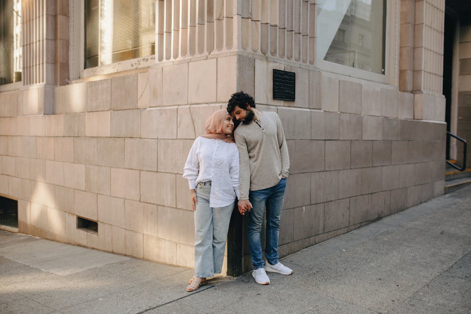 A loving couple stands and holds hands outside an urban building, showcasing a tender moment.