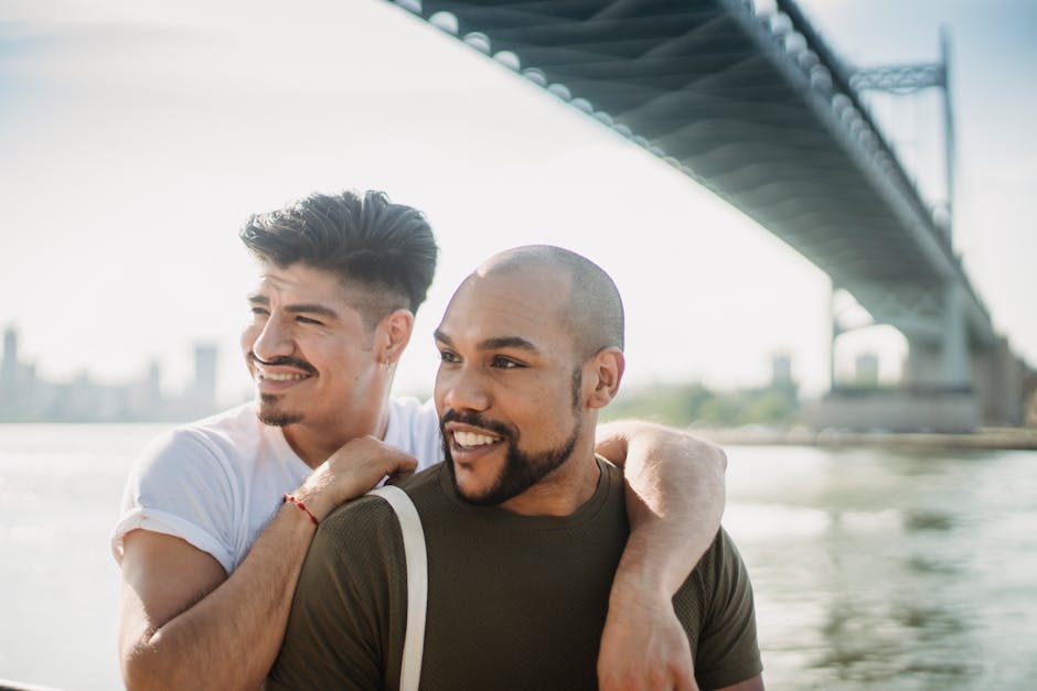 Joyful gay couple embracing under a city bridge on a sunny day.