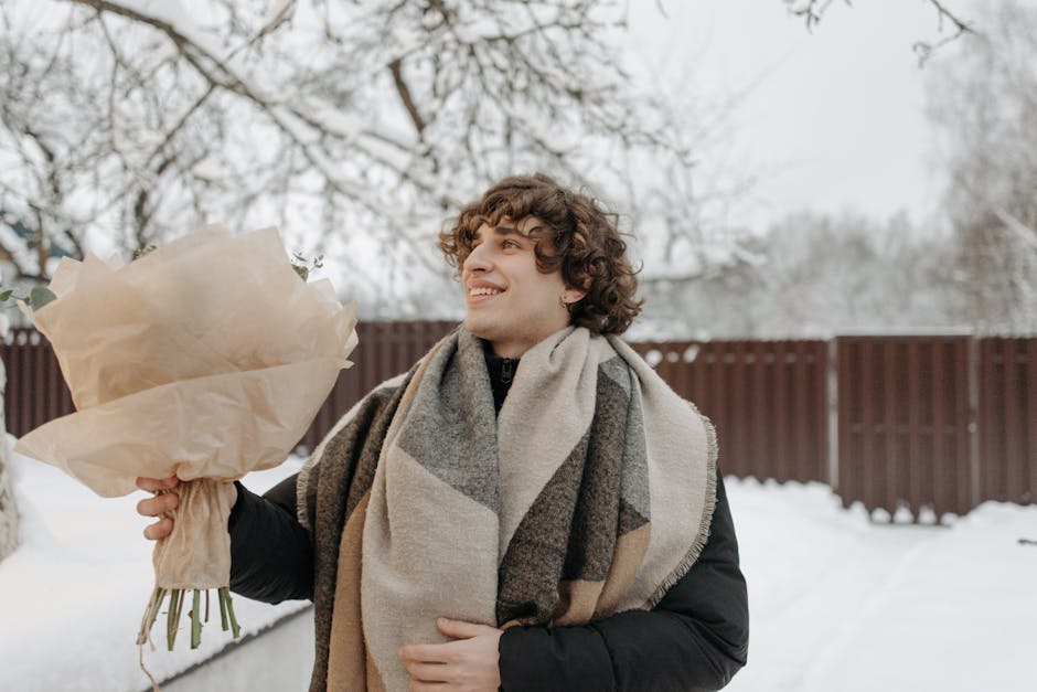 A man smiles warmly while holding a bouquet outdoors in a snowy winter setting.