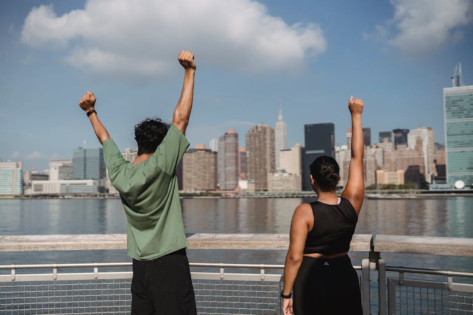 A joyful couple raises their hands in celebration facing a stunning city skyline.