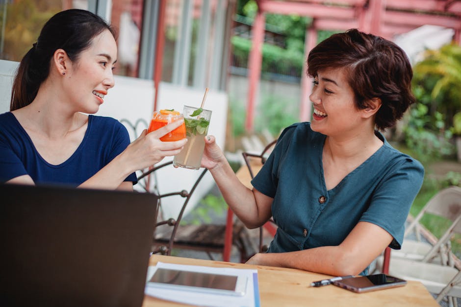 Two women clink glasses at an outdoor business meeting, symbolizing collaboration.
