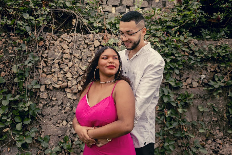 A loving couple shares a tender moment outdoors against a stony wall with foliage.