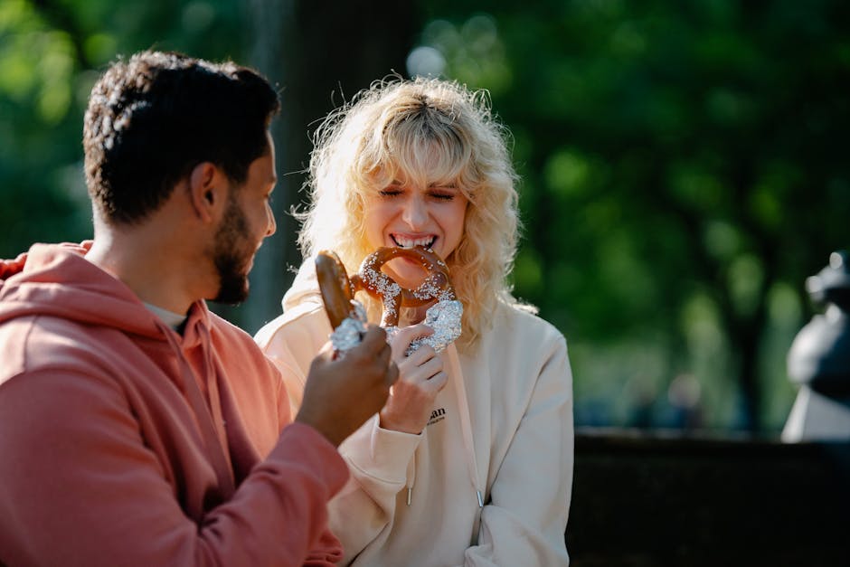 A happy couple enjoys pretzels together on a sunny day outdoors, radiating joy and warmth.