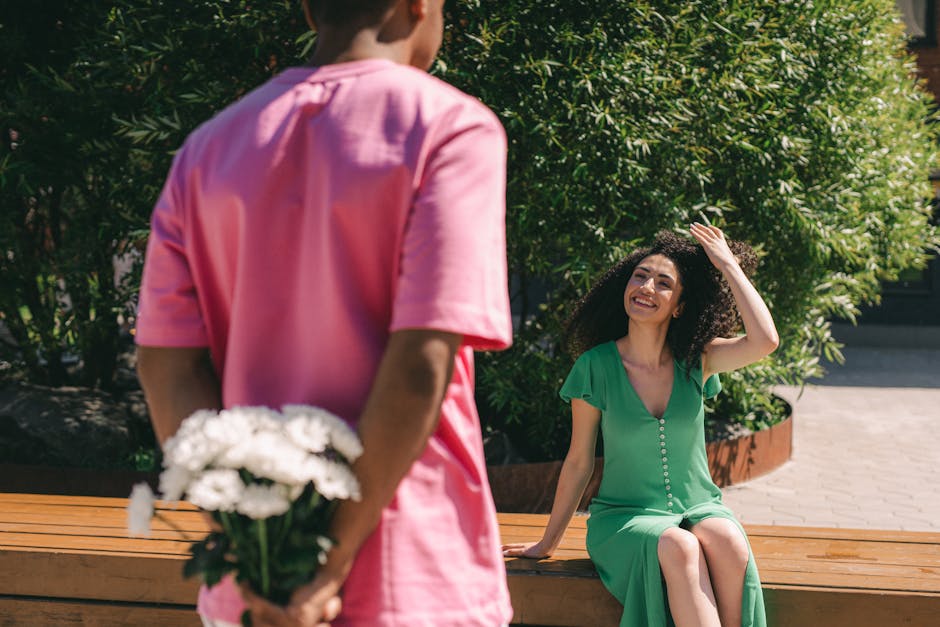 A man surprises a smiling woman with a bouquet of flowers outdoors, capturing a romantic moment.