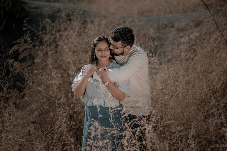 A couple shares a tender embrace in a sunlit field, capturing a moment of love and connection.