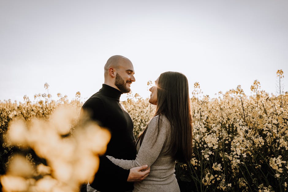 A couple enjoys a warm embrace in a field of flowers, under a clear sky, capturing a moment of love.