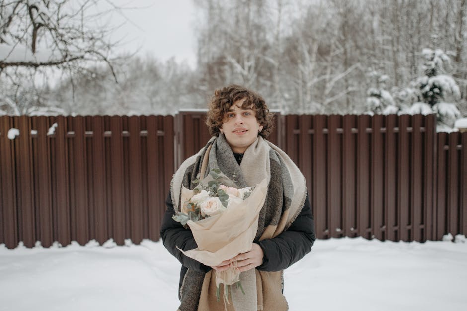 Young man standing outdoors in snow holding a bouquet of flowers, creating a romantic winter atmosphere.