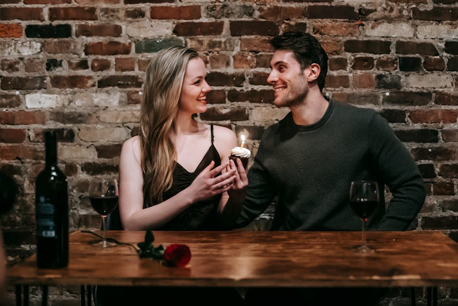 A joyful couple celebrating a special occasion with wine and a cupcake in a cozy restaurant setting.