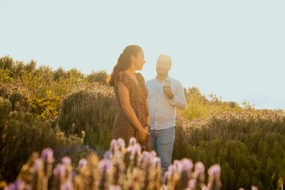 A couple embraces as a man proposes in a sunlit flower meadow during summer.