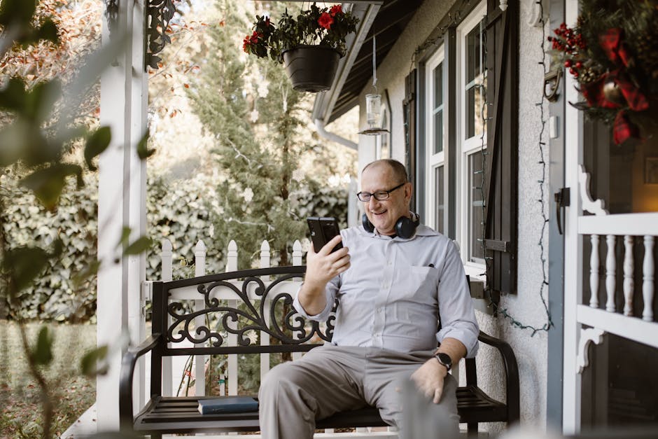 Senior man using phone and headphones for video call on home porch.