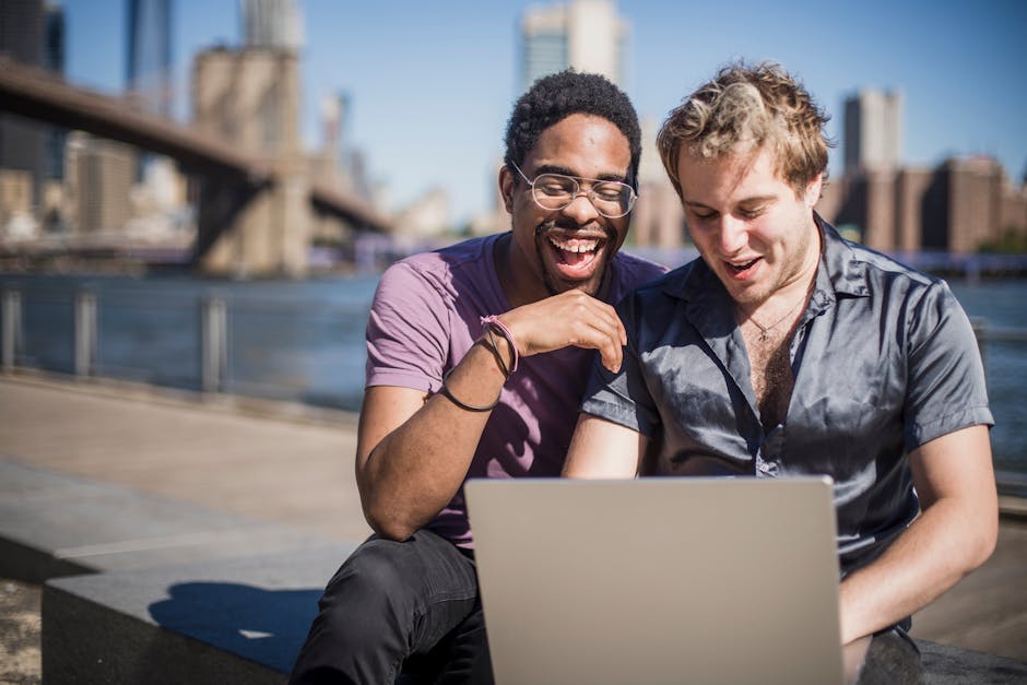 A joyful couple sitting outdoors by the river, using a laptop and enjoying each other's company.