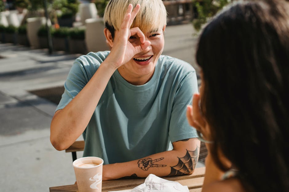 Happy young ethnic boyfriend smiling happily demonstrating ok sign to girlfriend while having coffee