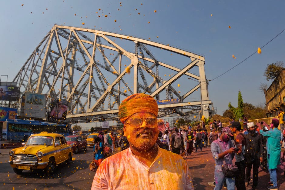 Vibrant Holi festival celebration near Howrah Bridge, Kolkata, with colorful powder in the air.