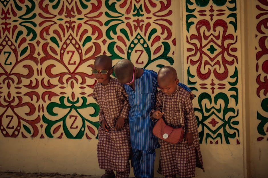 Three children pose in traditional attire against a vibrant decorative wall, showcasing cultural heritage.