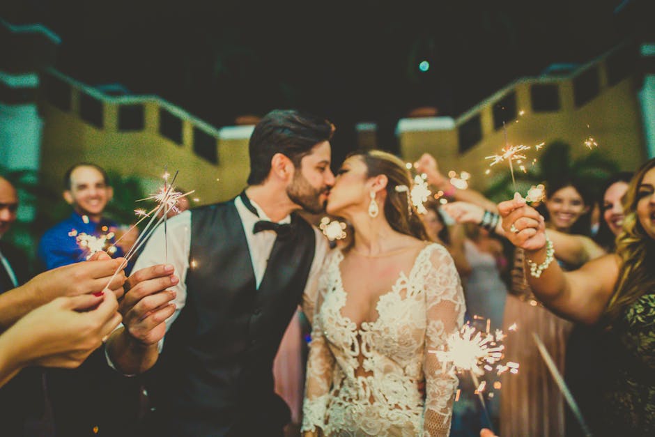 Bride and groom share a romantic kiss surrounded by sparklers at a wedding celebration.