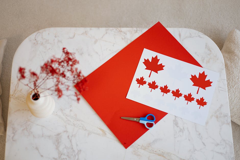 Top view of a Canadian flag craft project on a marble table with scissors and a vase.
