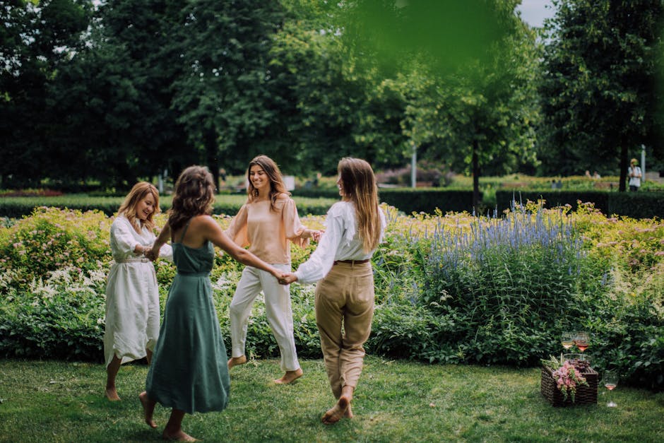 Four women dancing barefoot in a park, celebrating friendship with a joyful picnic.