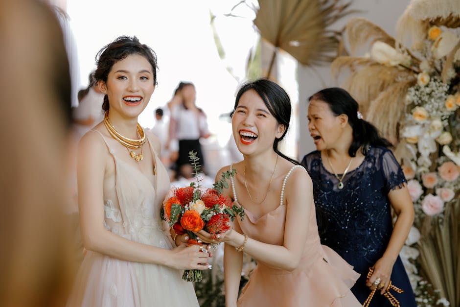 Bride and bridesmaid joyfully smiling at a wedding ceremony, holding a bouquet.
