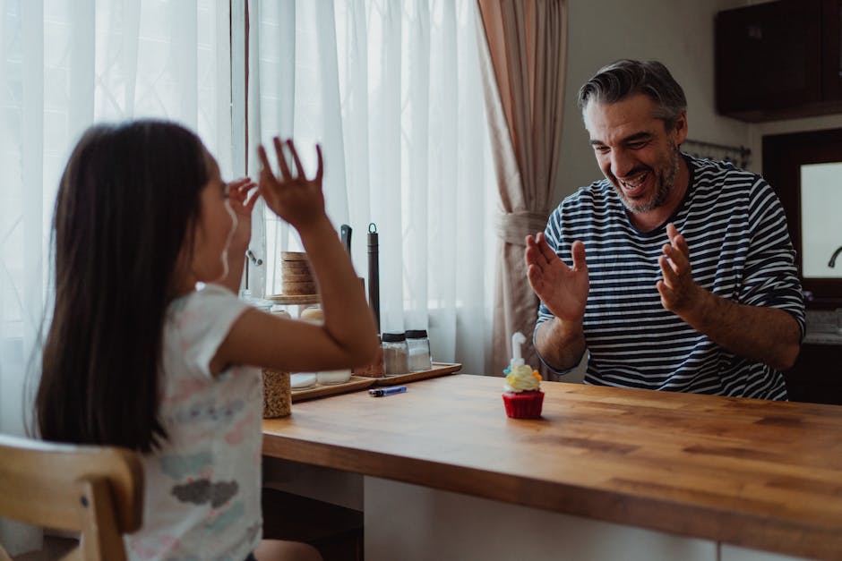 Father and daughter laughing and clapping at a cupcake in the kitchen during a joyful celebration.