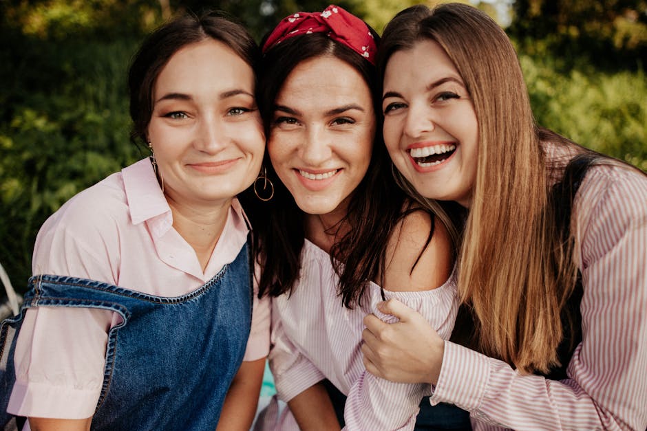 Three smiling friends embracing and laughing in a sunny outdoor setting, exuding happiness and friendship.