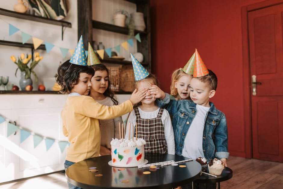 A group of cheerful children celebrating a birthday with cake and party hats indoors.