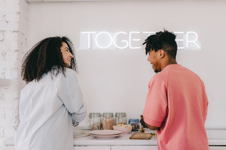 Two friends enjoy a light, cheerful moment preparing breakfast in a bright kitchen.