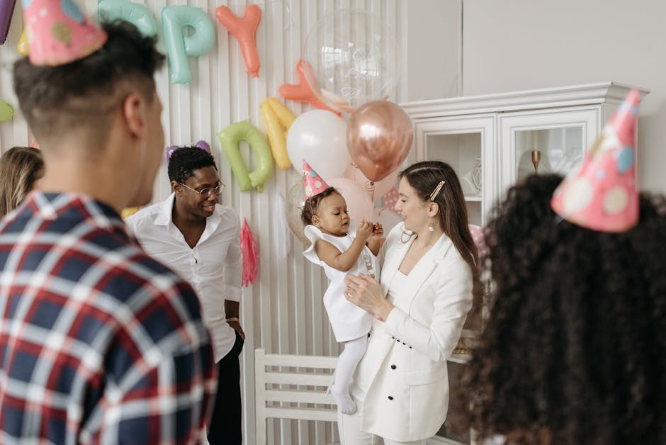 Joyful family and friends celebrating a child's birthday indoors with balloons and party hats.