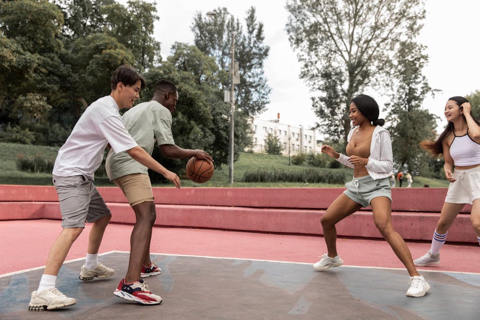 Diverse group of young adults playing a lively game of basketball on an outdoor court during the day.