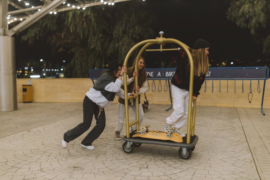 Three young women enjoying a playful night out, pushing a luggage cart outdoors.