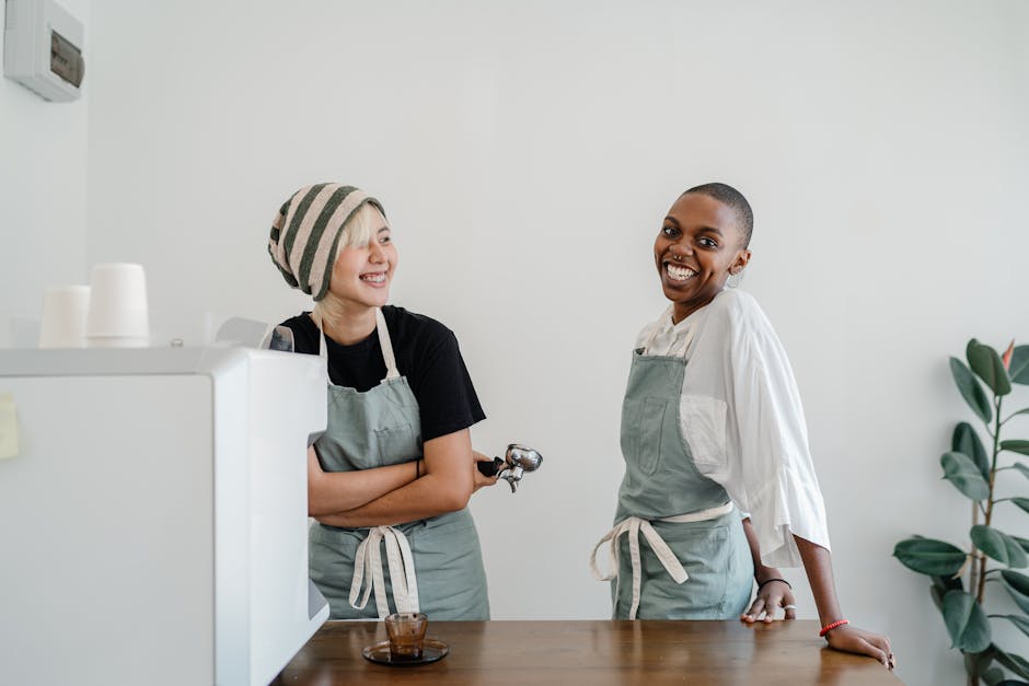 Two baristas in aprons share a laugh in a modern cafe, creating a friendly atmosphere.