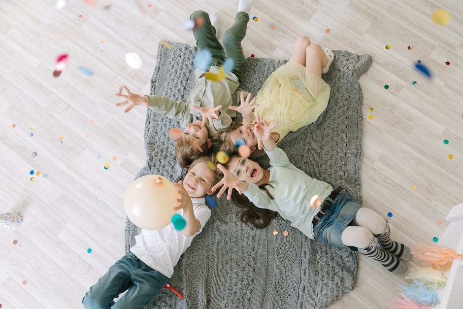 Aerial view of happy children celebrating with balloons and confetti indoors on a rug.