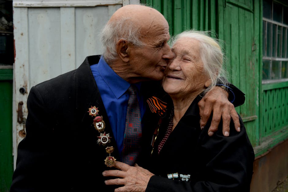 A senior couple sharing a loving embrace, adorned with medals, symbolizing enduring romance.